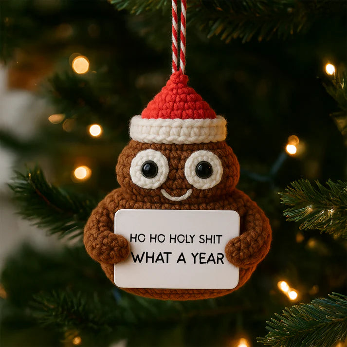Crocheted poop emoji ornament with a Santa hat holding a sign on a Christmas tree.