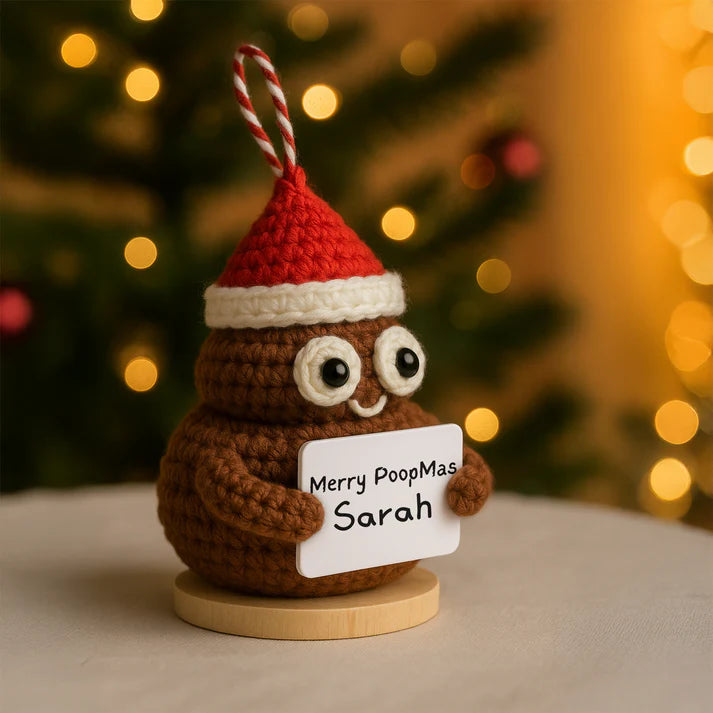 Crocheted poop emoji ornament with a Santa hat and 'Merry PoopMas Sarah' sign, Christmas tree in the background.