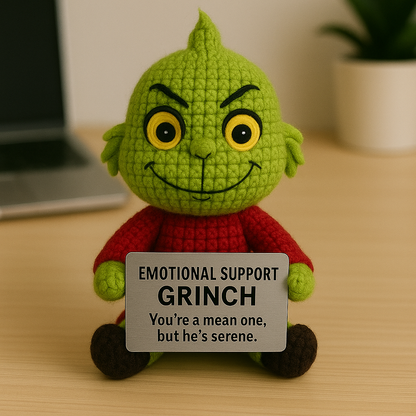 Green plush toy with a sign labeled 'Emotional Support Grinch' on a wooden surface.
